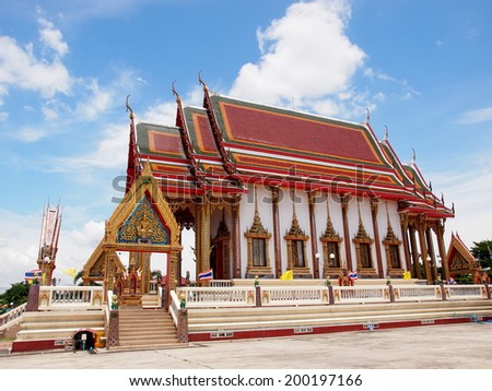 beautiful Thai temple building with stepping roof and rich of craft handmade decorative elements and ornaments in red and gold color outside under bright blue sky on a sunny day in Thailand 