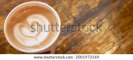 Table top view of a paper cup of hot latte coffee on wooden table. A latte is a coffee drink made with espresso and steamed milk.