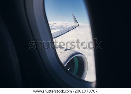 View through airplane window on wing with engine. Plane during flight above clouds. Royalty-Free Stock Photo #2001978707