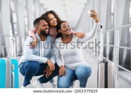 Ready For Adventures. Portrait Of Cheerful Young Black Family Taking Selfie With Smartphone In Airport Terminal Or On Railway Station, Tourists Posing At Camera Together, Blurrred Background