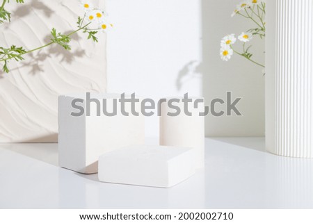Empty podium or pedestal with chamomile flowers on a white background. Blank shelf product standing background