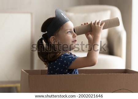 Adorable little Caucasian girl in pirate hat looking in spyglass, cute preschool child kid wearing homemade costume holding cardboard tube as telescope sitting in toy ship, playing funny game Royalty-Free Stock Photo #2002021646
