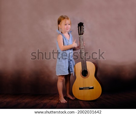 little girl holding a guitar and showing a super sign with the second hand on a vintage background.