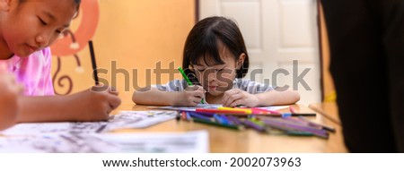 Asian little girl group sitting practice their skills and focus on coloring paper on table. Preschoolers learning at home to write and reading, Art education and creativity, Children's activities.