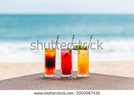 Bright Healthy Berries Cocktails on Table on Beach with Blue Sea on Background. Concept of Summer Vacations at Maldives or Caribbean Resorts. Fresh Fruit Ice Cold Drinks for Hot Weather Refreshment. Royalty-Free Stock Photo #2002087436