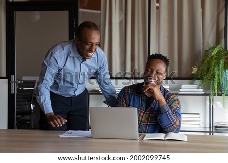 Excited African American colleagues working on project together, looking at laptop screen, happy executive mentor leader with employee discussing strategy, sharing ideas at meeting in office Royalty-Free Stock Photo #2002099745