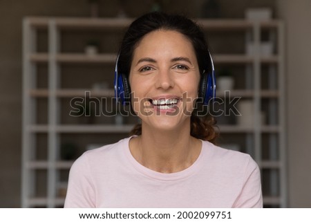 Smiling attractive millennial hispanic latin woman wearing wireless headphones looking at camera, holding pleasant video call conversation, communicating distantly with client or partners. Royalty-Free Stock Photo #2002099751