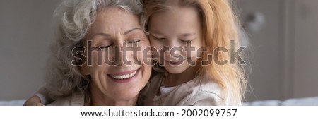 Happy faces of excited older grandmother and little preteen girl granddaughter cuddling after long separation touch cheeks with closed eyes feel love affection. Panoramic header image website banner