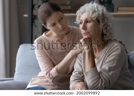 Young female caregiver support grieving suffering mature old woman retiree express empathy compassion. Supportive grown up daughter hug mature mother help overcome loss of beloved man health problem Royalty-Free Stock Photo #2002099892