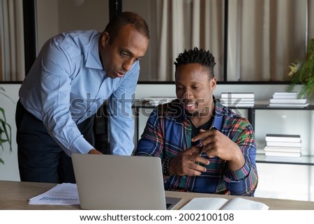 African American mentor teaching intern, pointing at laptop screen, executive manager leader instructing new employee, explaining strategy, colleagues working on online project in office together Royalty-Free Stock Photo #2002100108