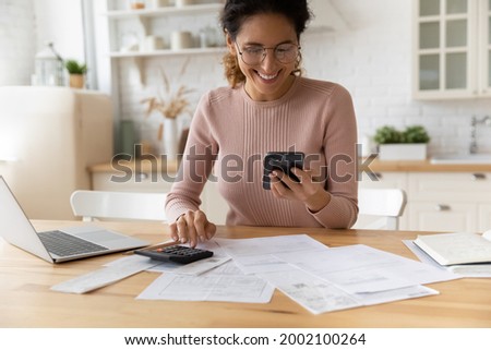 Smiling young 30s woman in eyewear looking at smartphone screen, feeling satisfied with fast secure online service, paying household bills taxes or insurance, managing budget, calculating expenses. Royalty-Free Stock Photo #2002100264