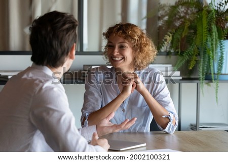Excited colleagues chatting discussing project ideas sitting at table, smiling businesswoman and businessman brainstorming talking in office, manager advisor consulting satisfied client at meeting Royalty-Free Stock Photo #2002100321