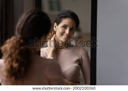 Rear back smiling 30s hispanic caucasian woman looking at mirror, checking appearance before leaving apartment, getting ready for job or walk, satisfied with neat fit look, admiring herself at home. Royalty-Free Stock Photo #2002100360