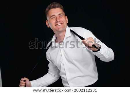 A handsome young man takes off his tie and laughs posing on a black background. A stylish business man. A big businessman.
