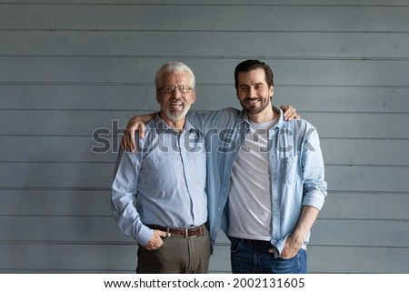Happy mature senior 70s father and grown son standing together, hugging, looking at camera with happy smile. Men of two generations head shot portrait. Family relations, fatherhood concept Royalty-Free Stock Photo #2002131605