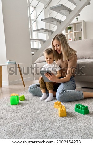 Smiling mum teaching toddler child using digital tablet at home. Happy family mom and kid holding pad computer, mother with small son virtual learning online, playing, having fun watching funny videos