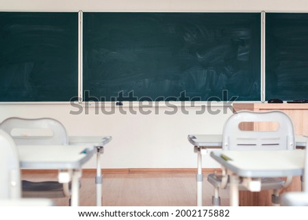 Empty school classroom. Green chalkboard on the wall. Education concept. Blackboard, desks and chairs in the class. Classroom of elementary school without students and teacher. Back to school.