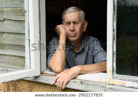 Portrait of an elderly man of 80 years old, sad looks from the window of an old house.  Royalty-Free Stock Photo #2002177835