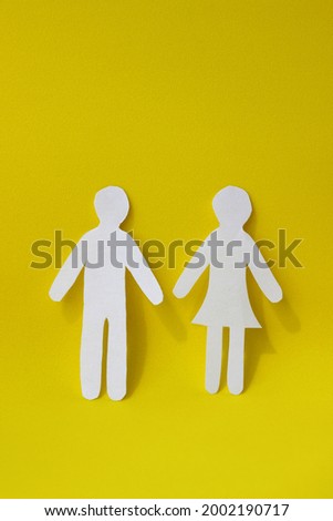 Silhouettes of a man and a woman are carved from white paper, standing side by side on a yellow background. The concept of love, relationships, family. Minimalistic vertical photo