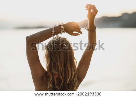 Rear view of an attractive young woman having fun and enjoying summer sunset on the beach.