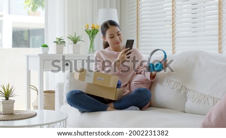 Young asia people happy teen girl smile unbox open gift new headphone buy order from online store shop take photo shoot camera show post social media app blog vlog share sit relax at home sofa couch. Royalty-Free Stock Photo #2002231382