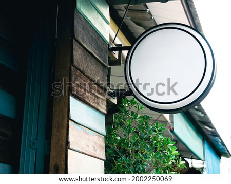 Round white blank shop sign. Mockup of circle hanging light box signage in front of restaurant, mounted on the old vintage wooden wall. Street signboard template.