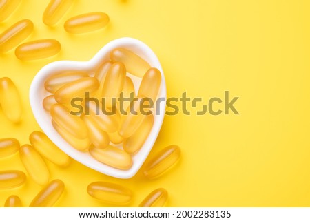 Vitamin D and Omega 3 fish oil capsules supplement in a heart-shaped plate on yellow background. Concept of healthcare. Top view - Image