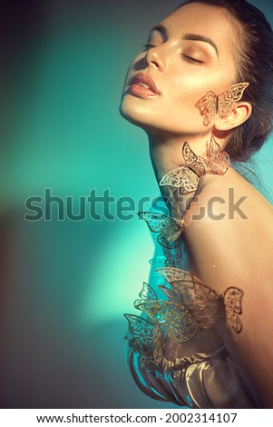 Beauty model girl in colorful bright neon lights posing, fashion make up with butterfly. Portrait of beautiful summer young woman in UV. Art design colorful make up with golden butterflies. 