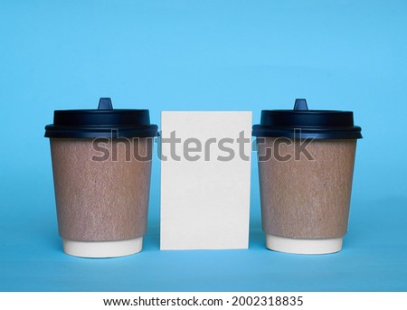 Two paper cups for coffee and a white cardboard card on a blue background. Mock up. Copy space