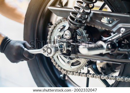 Mechanic using a wrench and socket to Remove and Replace Rear Motorcycle Wheel  , maintenance, repair motorcycle concept in garage .selective focus Royalty-Free Stock Photo #2002332047