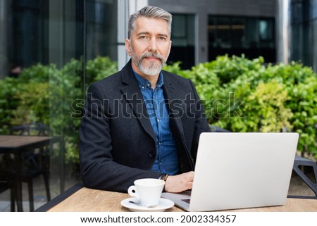 Mature man using laptop computer in a city cafe. Handsome middle age man working outdoors. Modern lifestyle, active seniors, connection, technology, people, business concept