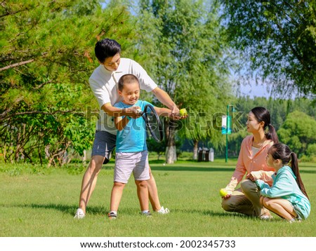Happy family of four playing tennis in the park high quality photo