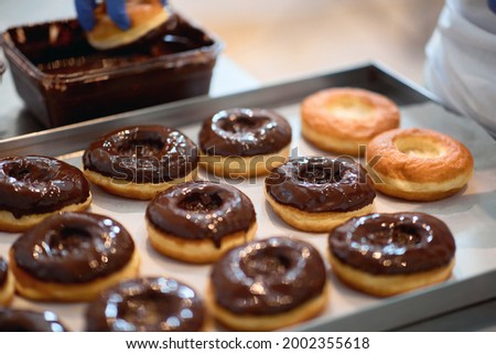 A worker is topping donuts with chocolate topping in a working atmosphere in a candy workshop. Pastry, dessert, sweet, making Royalty-Free Stock Photo #2002355618