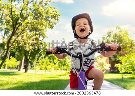 Portrait little cute adorable caucasian toddler boy in safety helmet enjoy having fun riding exercise bike in city park road yard garden forest. Child first bike. Kid outdoors sport summer activities Royalty-Free Stock Photo #2002363478