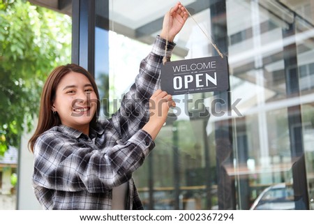 Happy waitress woman turning open sign board on glass door coffee shop.