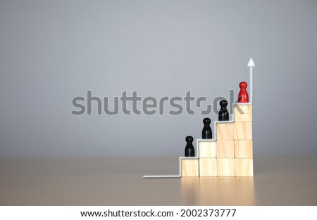 wooden doll in a hierarchy of wooden blocks. The concept of raising the level of individuals in the organization,  Leadership,  teamwork. with copy space for text or design concept for business  Royalty-Free Stock Photo #2002373777