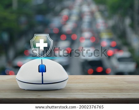 Cross shape with shield flat icon on wireless computer mouse on wooden table over blur of rush hour with cars and road in city, Business healthy and medical care insurance online concept