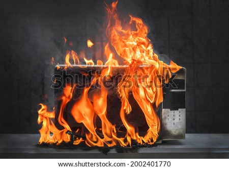 Microwave oven white, in fire front view, electrical appliances caught fire as a result of improper operation Royalty-Free Stock Photo #2002401770