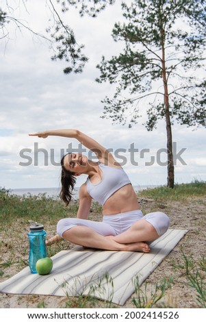 young woman sitting with crossed legs and stretching in forest