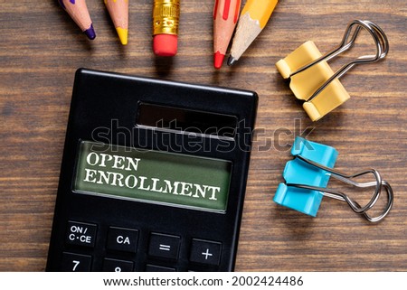 Open Enrollment. Calculator and office supplies on a wooden table.