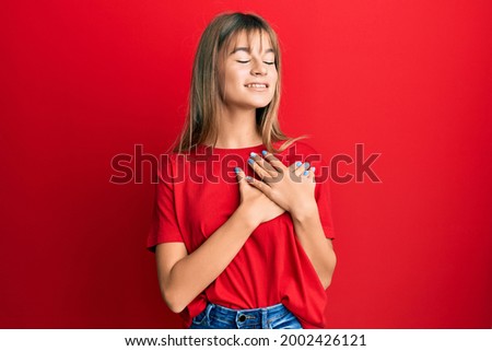 Teenager caucasian girl wearing casual red t shirt smiling with hands on chest, eyes closed with grateful gesture on face. health concept. 
