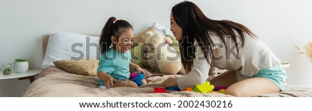 Asian mother and excited kid playing building blocks on bed, banner