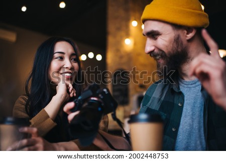 Successful professional photographers in trendy clothing sitting in cafeteria and discussing ideas for creating pictures content enjoying collaboration, happy hipster guys with slr camera communicate