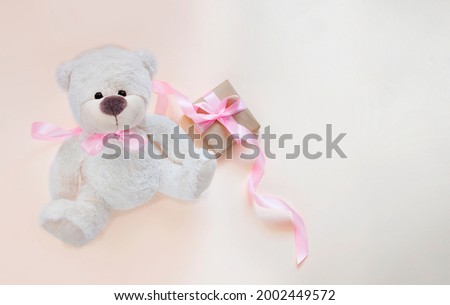 White teddy bear and present with pink silk ribbon on pale background. Image with copy space
