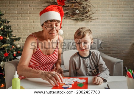 A Little boy with grandmother make Christmas craft, greeting card. Christmas tree and decoration on background.