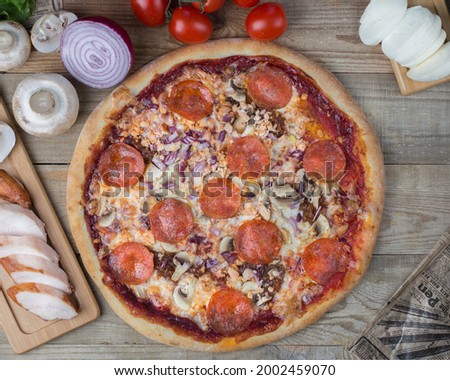 Pizza with pepperoni, smoked chicken, red onion, mozzarella, tomato sauce and tomatoes on a light wooden background.