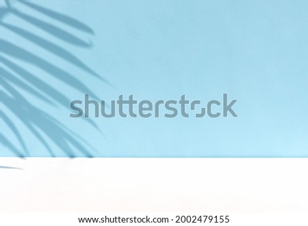 Minimal abstract background for the presentation of a cosmetic product. Premium podium with a shadow of tropical palm leaves on a pastel blue wall and white table. Showcase, display case.