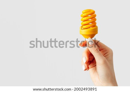 Female hand holding light bulb against gray background