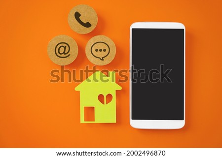 white mobile phone, green house paper cut and contact method sign on vivid orange background  contact us,  , question and answer ,new normal lifestyle , social distancing ,work from home
