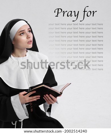 Young praying nun with Bible on light background with space for text